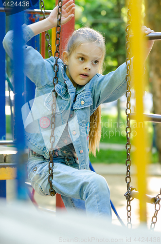 Image of The girl tries to climb from one hanging ladder to another on the playground