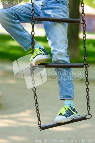 Image of Legs of a child in sneakers with light green laces on a metal ladder on chains