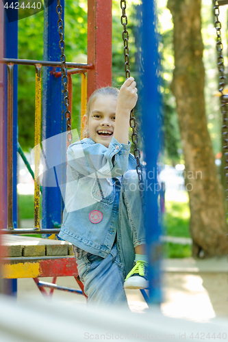 Image of The girl joyfully and fervently laughs sitting on a hanging ladder in the playground