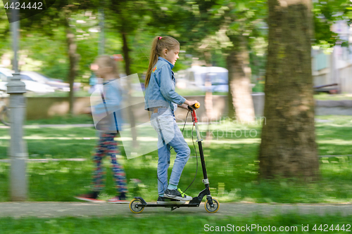 Image of The girl is happily riding a scooter along an asphalt road