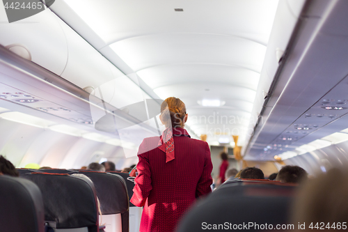 Image of Stewardess in red uniform walking the aisle of commercial airplane.