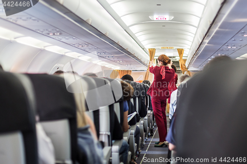 Image of Stewardess in red uniform giving safety instructions on commercial passengers airplane.