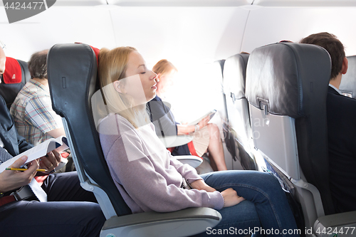 Image of Tired blonde casual caucasian lady napping on seat while traveling by airplane. Commercial transportation by planes.