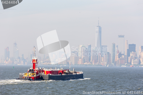 Image of Freight tug pushing cargo ship to the port in New York City and Lower Manhattan skyscarpers skyline in background.