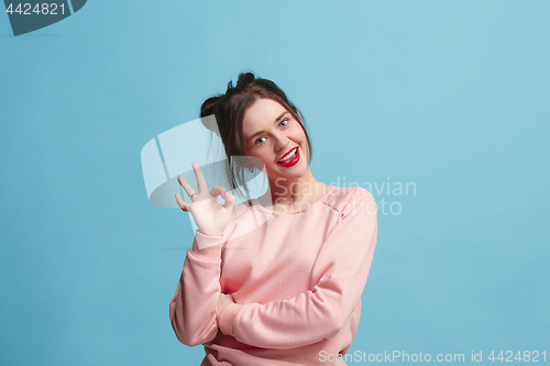 Image of The happy business woman standing and smiling against blue background with sign ok.