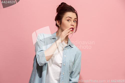 Image of The young woman whispering a secret behind her hand over pink background