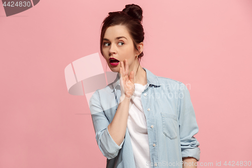 Image of The young woman whispering a secret behind her hand over pink background