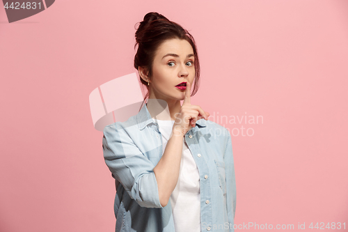 Image of The young woman whispering a secret behind her hand over pink background