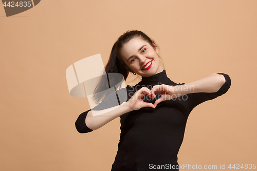 Image of Portrait of attractive cute girl with bright makeup smiling with a heart isolated over pastel background