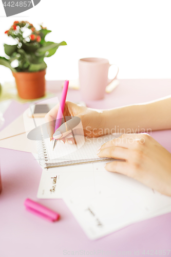 Image of The female hands holding pen. The phone on trendy pink desk.