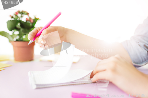 Image of The female hands holding pen. The phone on trendy pink desk.