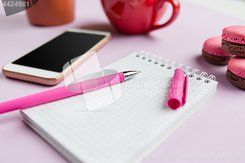 Image of The side view on female desk. The phone and french macarons on trendy pink desk.