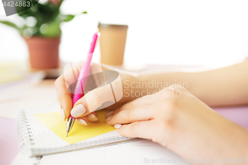 Image of The female hands holding pen. The phone on trendy pink desk.