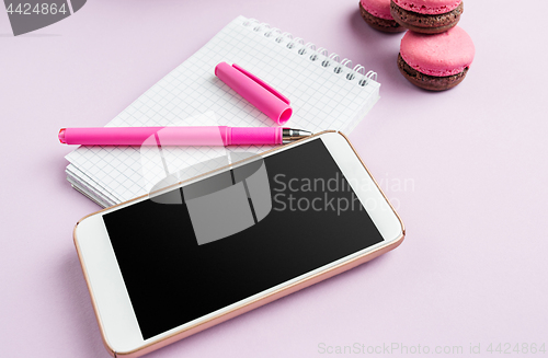 Image of The side view on female desk. The phone and french macarons on trendy pink desk.