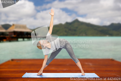 Image of woman making yoga triangle pose on mat outdoors