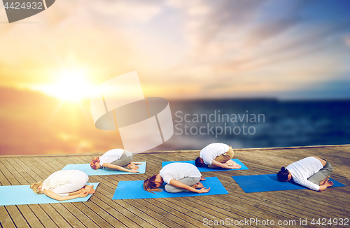 Image of group of people doing yoga child pose outdoors