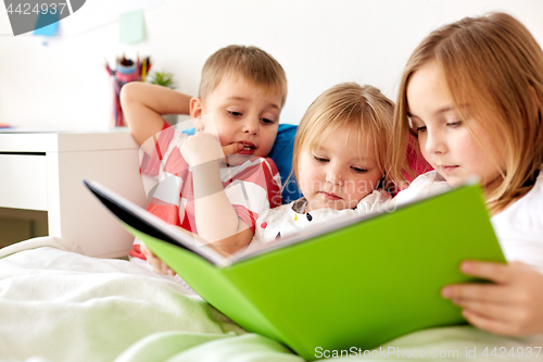 Image of little kids reading book in bed at home