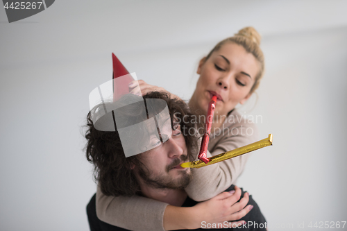 Image of couple in party hats blowing in whistle