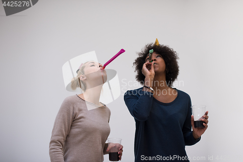 Image of smiling women in party caps blowing to whistles