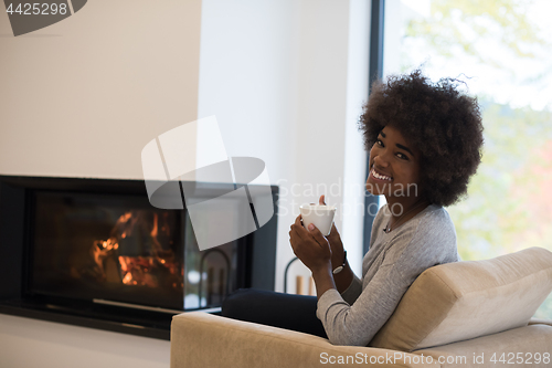 Image of black woman drinking coffee in front of fireplace