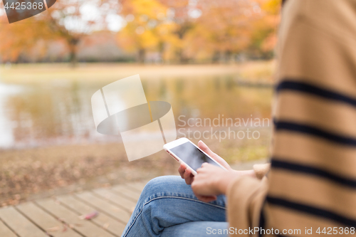 Image of Woman using cellphone in the park in autumn season