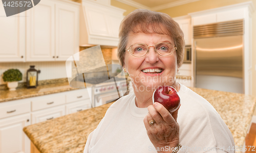 Image of Happy Senior Adult Woman with Red Apple Inside Kitchen.