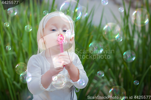 Image of Adorable Little Girl Sitting On Bench Having Fun With Blowing Bu