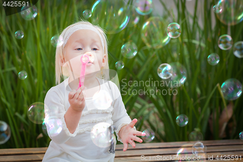 Image of Adorable Little Girl Sitting On Bench Having Fun With Blowing Bu