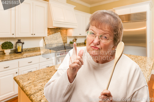 Image of Senior Adult Woman Scolding with The Wooden Spoon Inside Kitchen