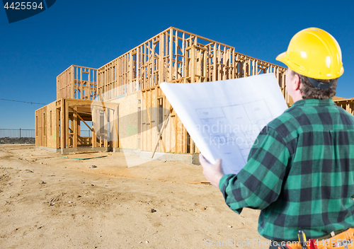 Image of Contractor with Plans and Hard Hat Looking At New House Framing 