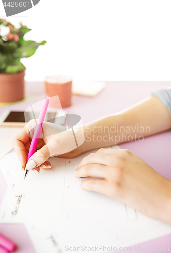 Image of The female hands holding pen. The phone on trendy pink desk.