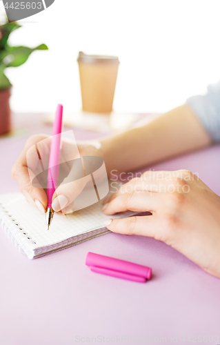 Image of The female hands holding pen. The phone on trendy pink desk.