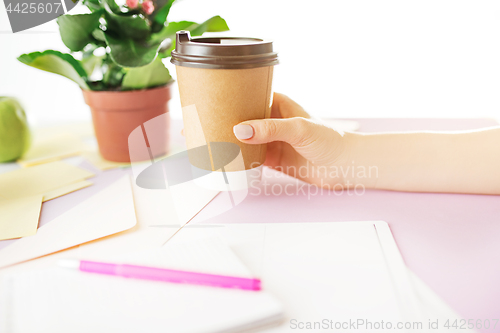 Image of The female hands holding coffee on trendy pink desk.