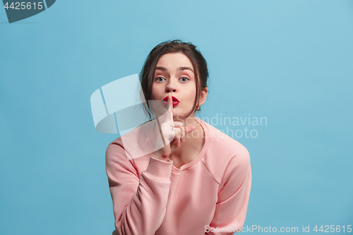 Image of The young woman whispering a secret behind her hand over blue background