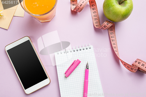 Image of Top view of green apple, measuring tape, mobile phone, pen and open notebook. Fitness Concept.