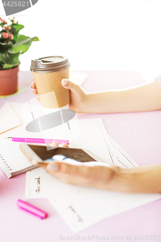 Image of The female hands holding phone and coffee on trendy pink desk.