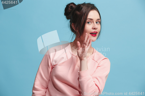 Image of The young woman whispering a secret behind her hand over blue background