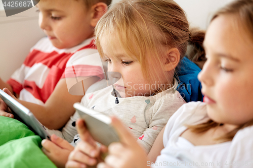 Image of kids with tablet pc and smartphone in bed at home