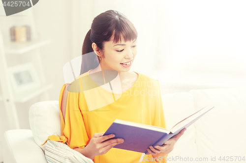 Image of smiling young asian woman reading book at home