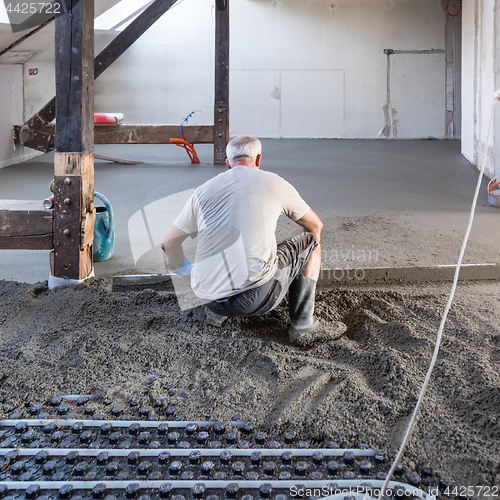 Image of Laborer leveling sand and cement screed over floor heating.