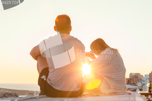 Image of Couple watching sunrise and taking vacation photos at Santorini island, Greece.