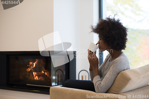 Image of black woman drinking coffee in front of fireplace