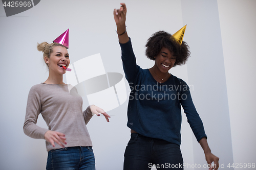 Image of smiling women in party caps blowing to whistles