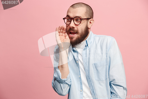 Image of The young man whispering a secret behind her hand over pink background