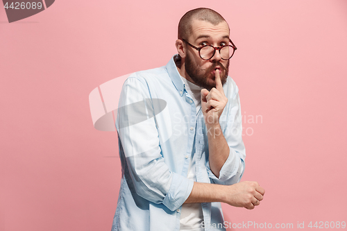 Image of The young man whispering a secret behind her hand over pink background
