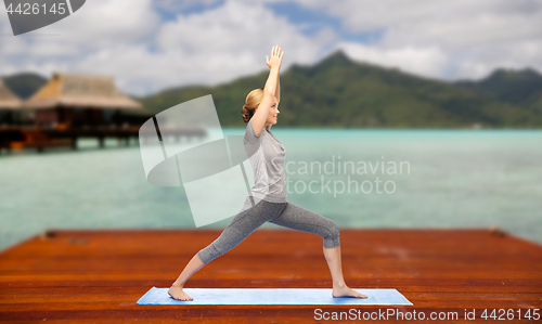 Image of woman making yoga warrior pose on mat outdoors