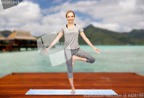 Image of woman making yoga in tree pose on mat outdoors