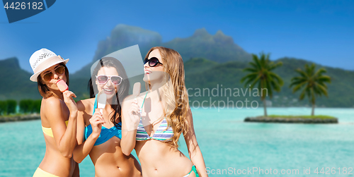 Image of group of smiling women eating ice cream on beach