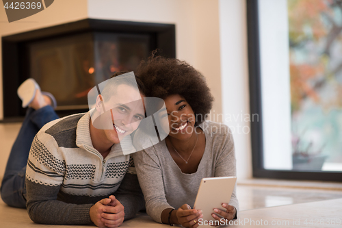 Image of multiethnic couple using tablet computer on the floor