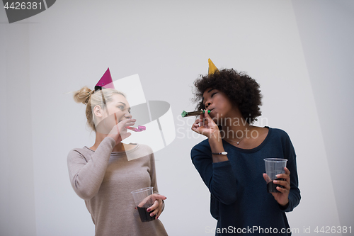 Image of smiling women in party caps blowing to whistles